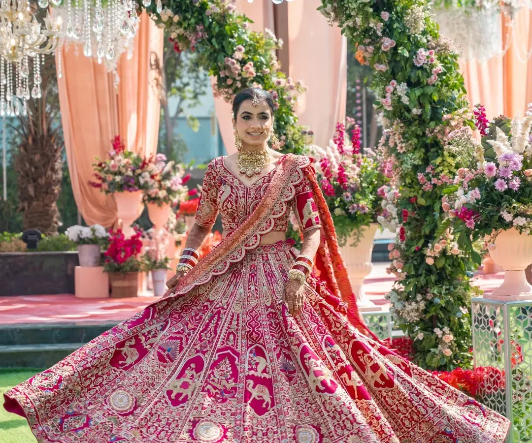 A classic bridal twirl showcasing the magnificent red lehenga against a backdrop of lush floral arches. This portrait captures the grace and happiness of the bride on her special day.