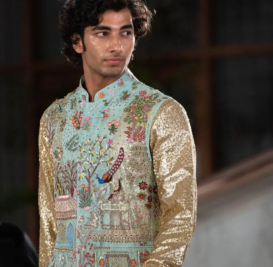 This is where art meets fashion. A model presents a stunning, custom-embroidered bandhgala jacket featuring intricate motifs of peacocks and architecture, paired with sparkling sequin sleeves for a truly one-of-a-kind statement piece.