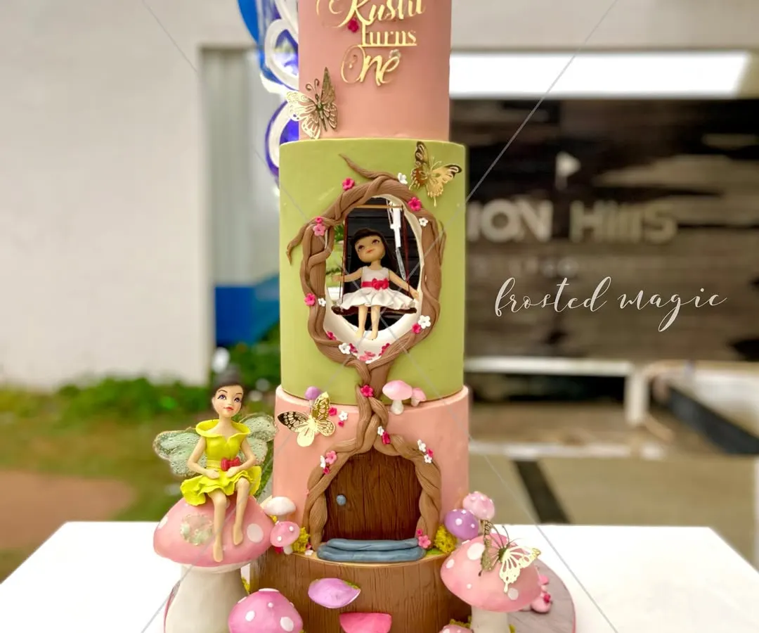 For a little princess's first birthday, I created this three-tiered enchanted fairy house cake. Every element, including the little girl on the swing and the fairy perched on a mushroom, is completely handmade from fondant to bring this magical world to life.