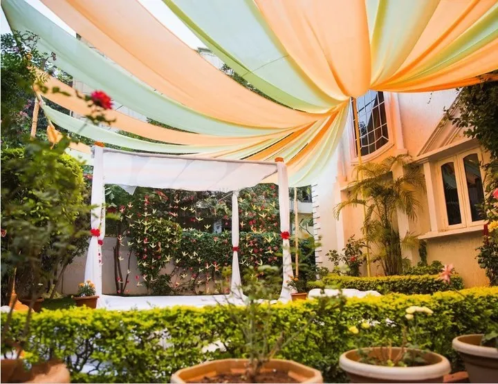We transformed this home garden into a serene sanctuary for an intimate wedding ceremony. A simple white mandap is framed by flowing pastel drapes in mint green and soft peach, creating a dreamy canopy overhead. This design showcases our ability to create an elegant and romantic atmosphere using fabric and the natural beauty of your home's surroundings.