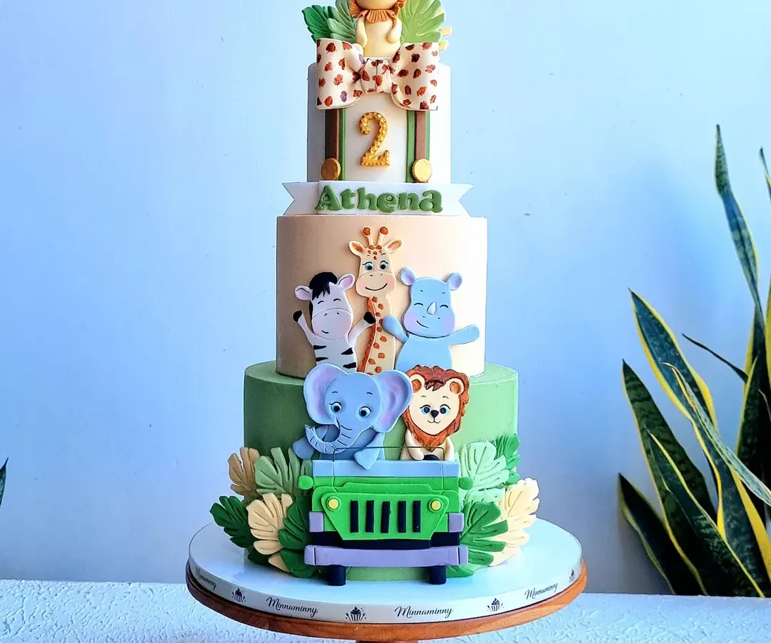 A grand three-tier safari adventure cake, perfect for a milestone birthday. This design features a whole crew of friendly, handmade fondant animals like a lion, elephant, and giraffe in a jeep, set against a backdrop of fondant leaves, creating a fun jungle expedition theme.