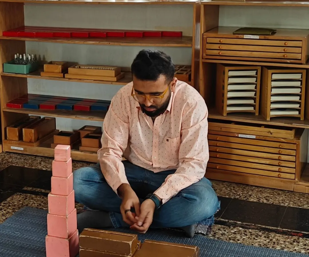 A father deeply focused on the iconic Montessori Pink Tower. In our Silent Journey workshops, parents work with the materials themselves to gain a profound, first hand understanding of their child's world of learning.