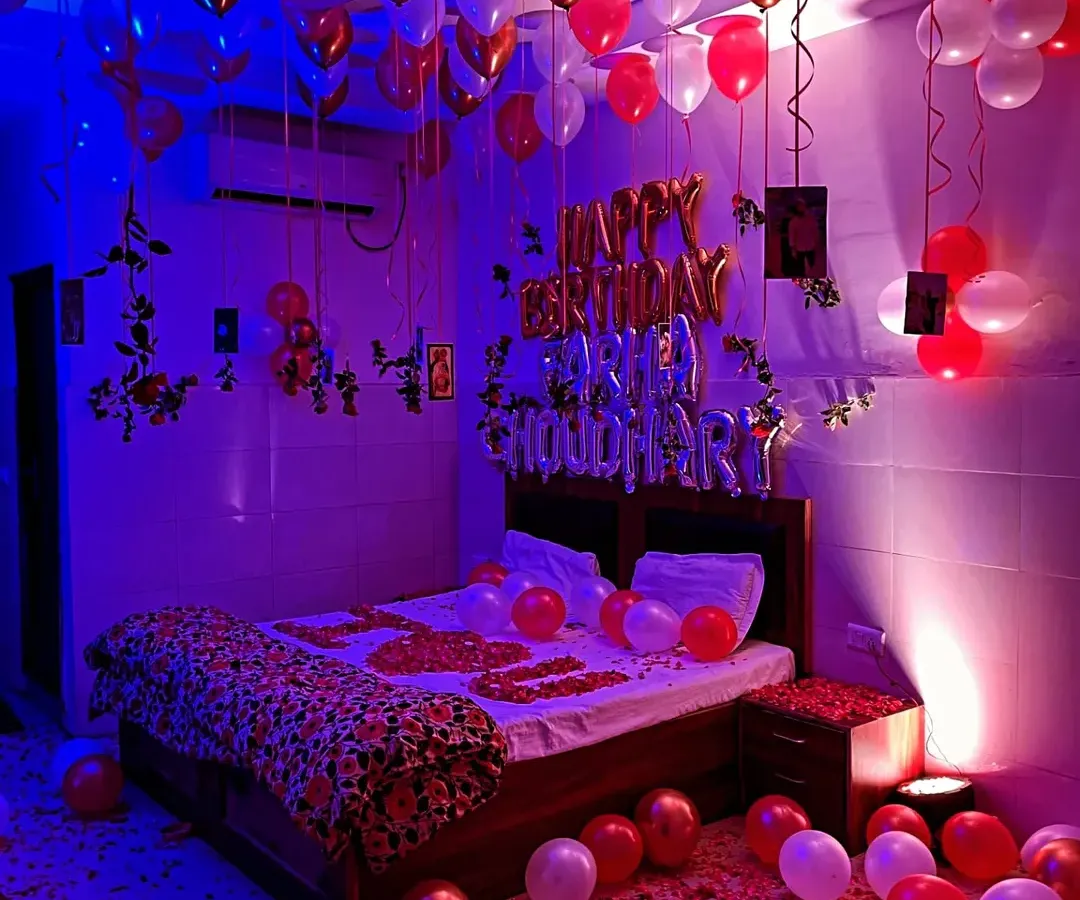 For this birthday surprise, I used moody blue and purple lighting to create a vibrant, celebratory atmosphere. The room is filled with red and white balloons on the ceiling and floor, with 'Happy Birthday' foil balloons and photos of the couple hanging above the bed.
