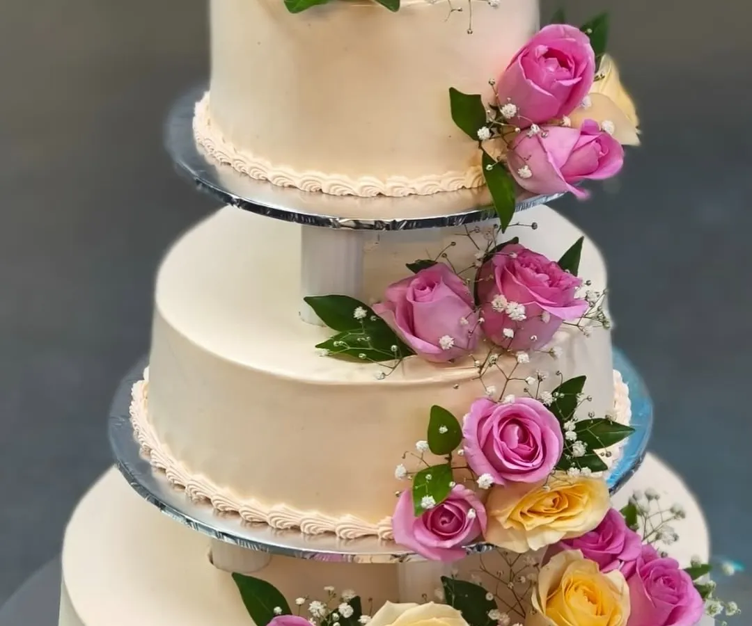 We believe your wedding cake should be as grand as your love story. This classic three-tiered cake, adorned with fresh pink and yellow roses, is a timeless centerpiece for any wedding celebration.