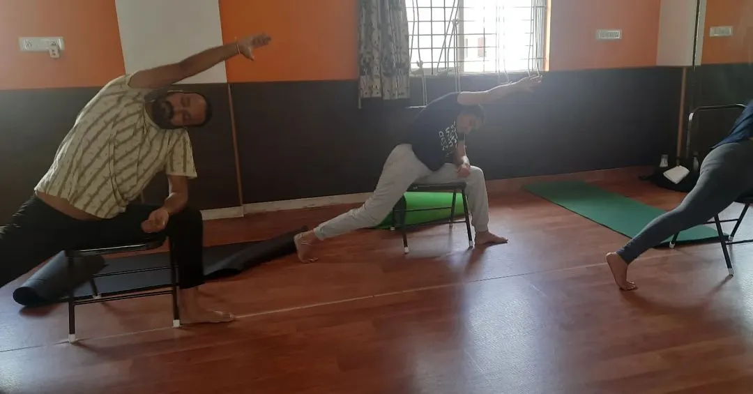 This is what a typical adaptive class looks like. We are using chairs to find stability and alignment in Virabhadrasana, or Warrior Pose. This modification makes the pose accessible for those with knee issues or balance concerns, allowing everyone to build strength safely.