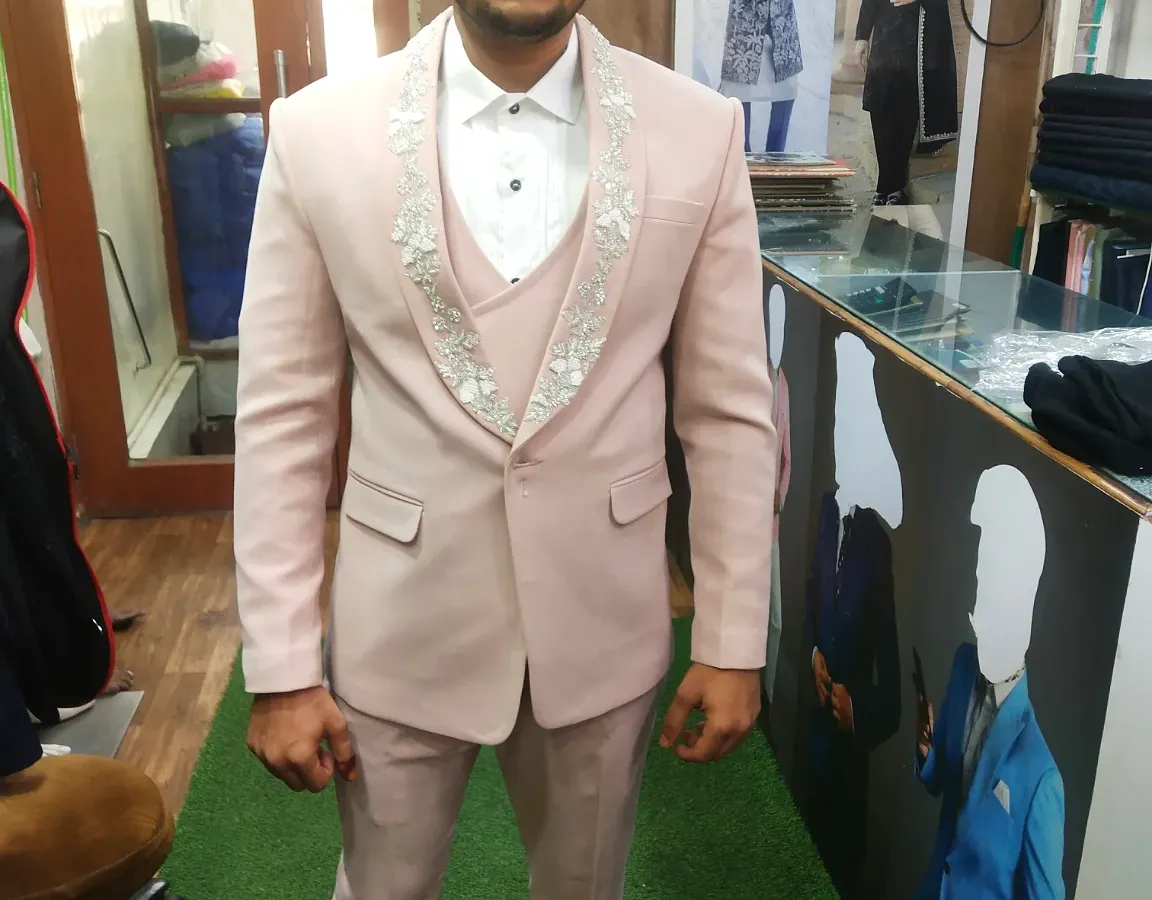 This client is seen during a fitting for his three-piece suit in a distinctive light pink fabric. The design includes detailed embroidery on the waistcoat and lapels, showcasing our ability to create unique, personalized groomswear.