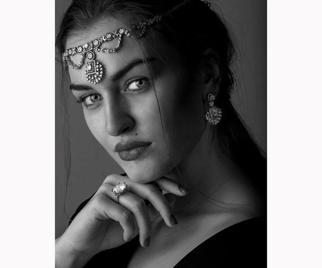 An intense black and white portrait for a jewellery campaign. The focus is on the model's direct gaze and the exquisite detail of the traditional headpiece and ring, captured with classic lighting to create a timeless and powerful image.