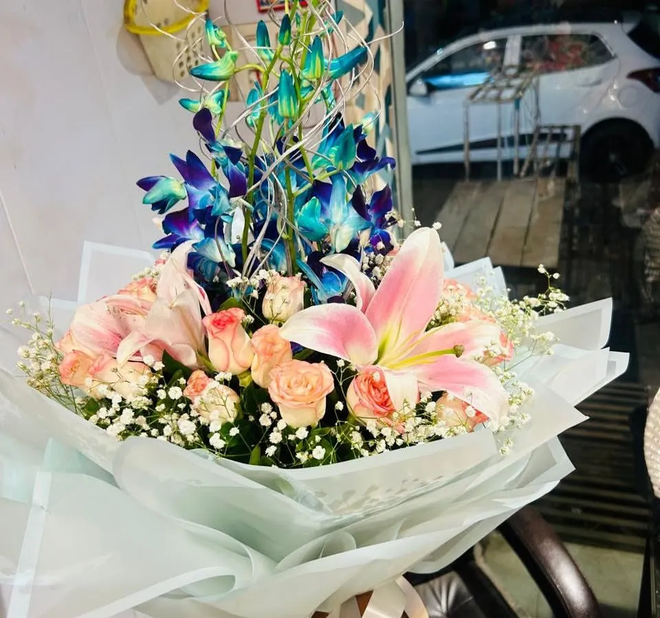 A premium hand-tied bouquet featuring vibrant blue orchids, soft pink lilies, and delicate peach roses. This is a great choice if you want a modern and elegant flower arrangement.