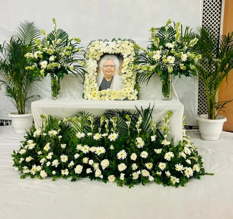 This is the kind of serene and respectful memorial setup I create for families. It features a central table with a beautiful photo frame garland made from fresh white flowers, flanked by elegant bouquets and lush green plants. I design these arrangements to bring a sense of peace and dignity to the service, ensuring every detail is handled with care.