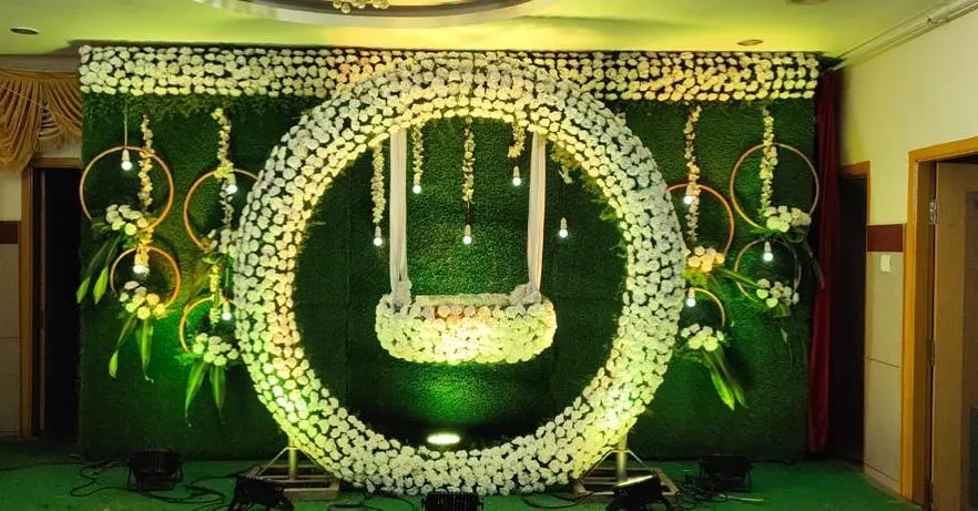 For a grand naming ceremony, we designed this stunning floral ring with a hanging cradle. This modern setup against a lush green wall creates a dramatic and beautiful centerpiece for the event.