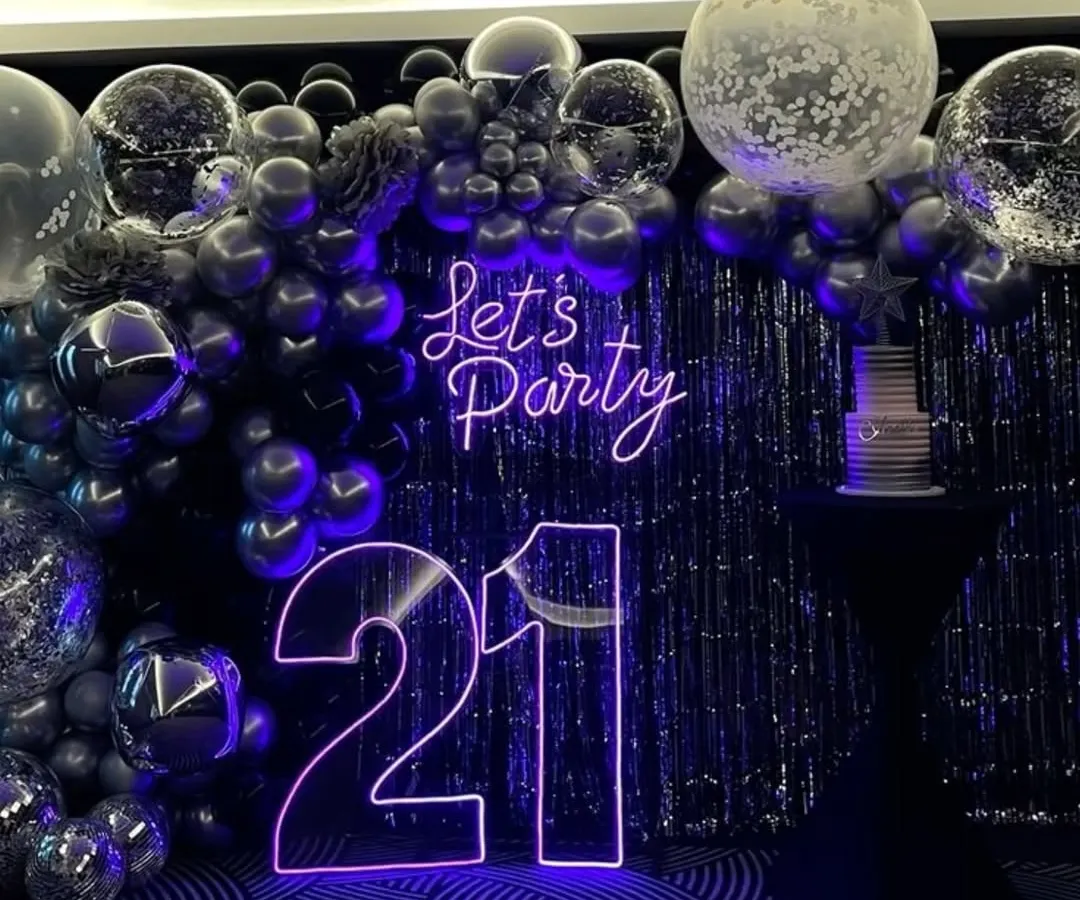 For this 21st birthday, we went for a chic and modern party vibe. The centerpiece is the glowing neon signage, including the age and a 'Let's Party' sign. I paired it with a dramatic backdrop of a silver tinsel curtain and a cascade of chrome and confetti balloons for a truly stylish celebration.