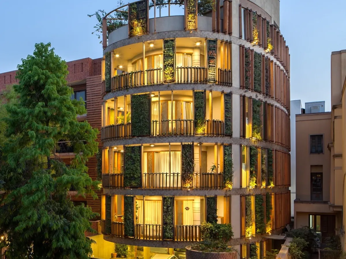 The Outré House in New Delhi, where handcrafted details and natural elements intertwine. The curved facade features a unique combination of precisely turned wooden louvres and vertical green walls, creating a living, breathing skin for the building.