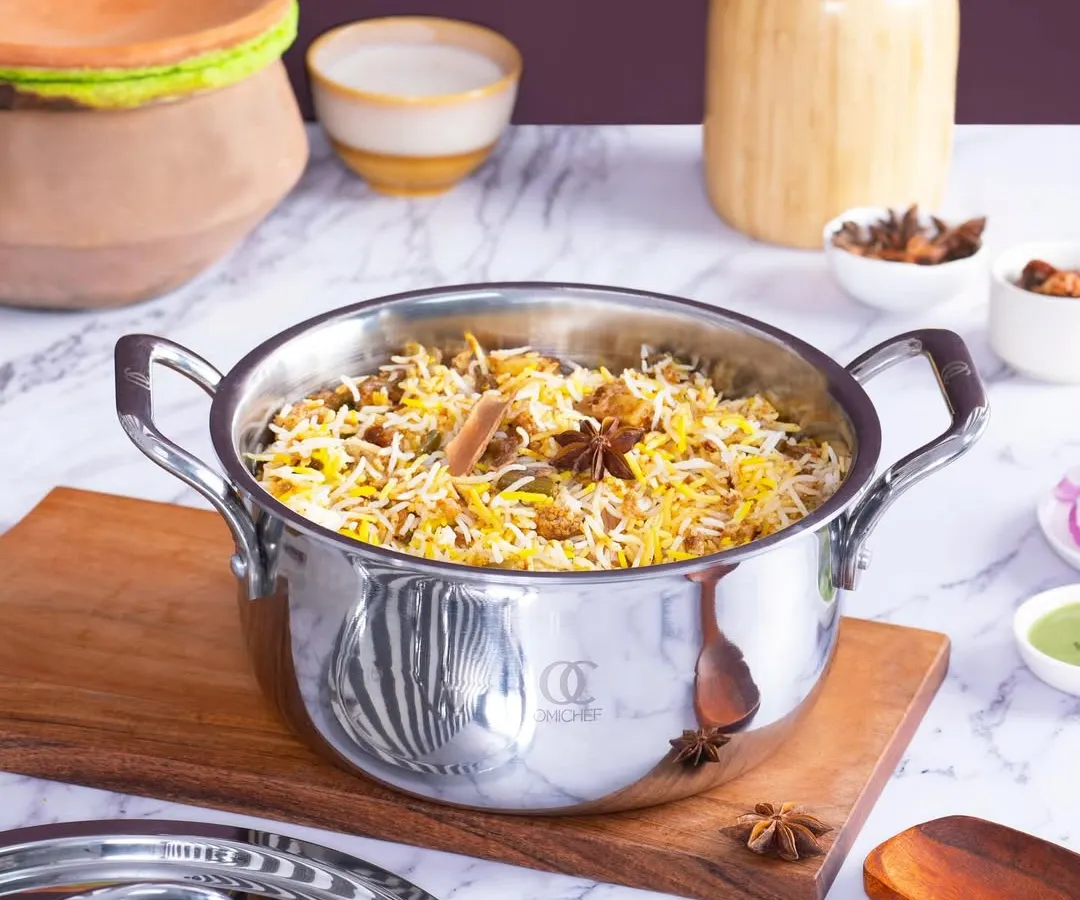 A lifestyle shot for Omichef's stainless steel cookware, featuring a freshly made biryani. The styling uses authentic ingredients like star anise to create an aromatic and tempting scene, highlighting the pot's capacity and quality for cooking traditional Indian dishes.