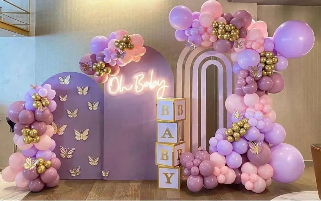 This pastel baby shower decoration is one of my most requested styles. It features custom-built lavender arched panels with delicate butterfly accents, an "Oh Baby" neon sign, and a stunning organic balloon garland in shades of lilac, pink, and gold. The stacked "BABY" blocks complete this elegant and modern photo-ready backdrop.
