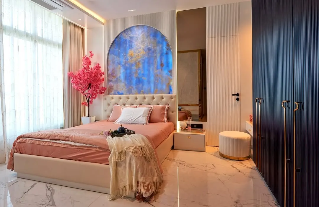 For this young client's bedroom, we created a sanctuary that reflects her personality. The design centers around a stunning blue stone arch, complemented by soft peach and white tones, while the deep blue fluted wardrobes add a touch of modern sophistication.