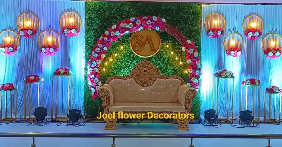 This modern engagement stage features a lush greenery wall with a circular floral arch and a custom 'SA' monogram. Hanging lanterns and spotlights add a warm, celebratory glow to the event.