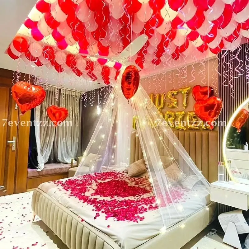 For a truly romantic first night or wedding surprise, I create setups like this one. It features a beautiful canopy over the bed with fairy lights, 'Just Married' foil balloons, and a ceiling full of red and white balloons. I also scatter fresh rose petals on the bed to complete the look.