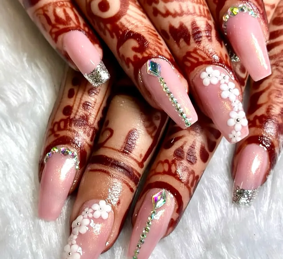 A perfect bridal manicure to complement intricate mehndi. This set features a soft pink base on coffin-shaped extensions, with delicate 3D white florals, silver glitter tips, and sparkling crystal accents for that ultimate wedding day glam.