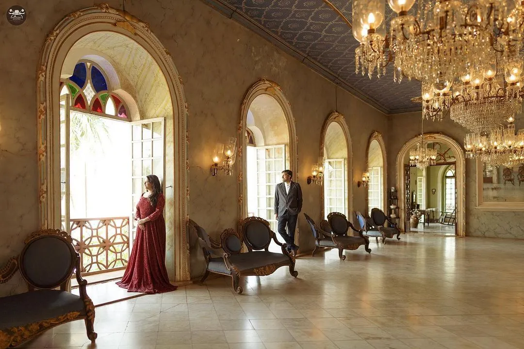 A couple stands framed in an ornate archway of a palace hall, with grand chandeliers and marble floors creating a sense of timeless elegance. This pre-wedding shoot in Hampi showcases how I use architectural elements to create stunning, regal portraits.