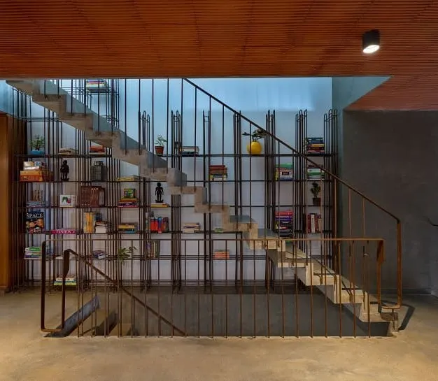 This statement staircase is a functional sculpture, with its concrete steps appearing to float against a backdrop of a floor-to-ceiling bookshelf made of slender metal rods. It's a design that integrates storage and circulation into a single, striking feature.