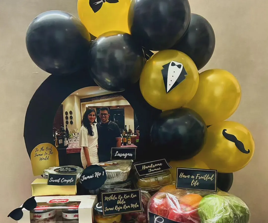 I created this luxurious "Jamai Raja" hamper to give the groom-to-be the royal treatment. It's packed with a mix of gourmet food platters like lasagna, fresh fruits, and sweets, all personalized with a photo and themed balloons in a sophisticated black and gold palette.