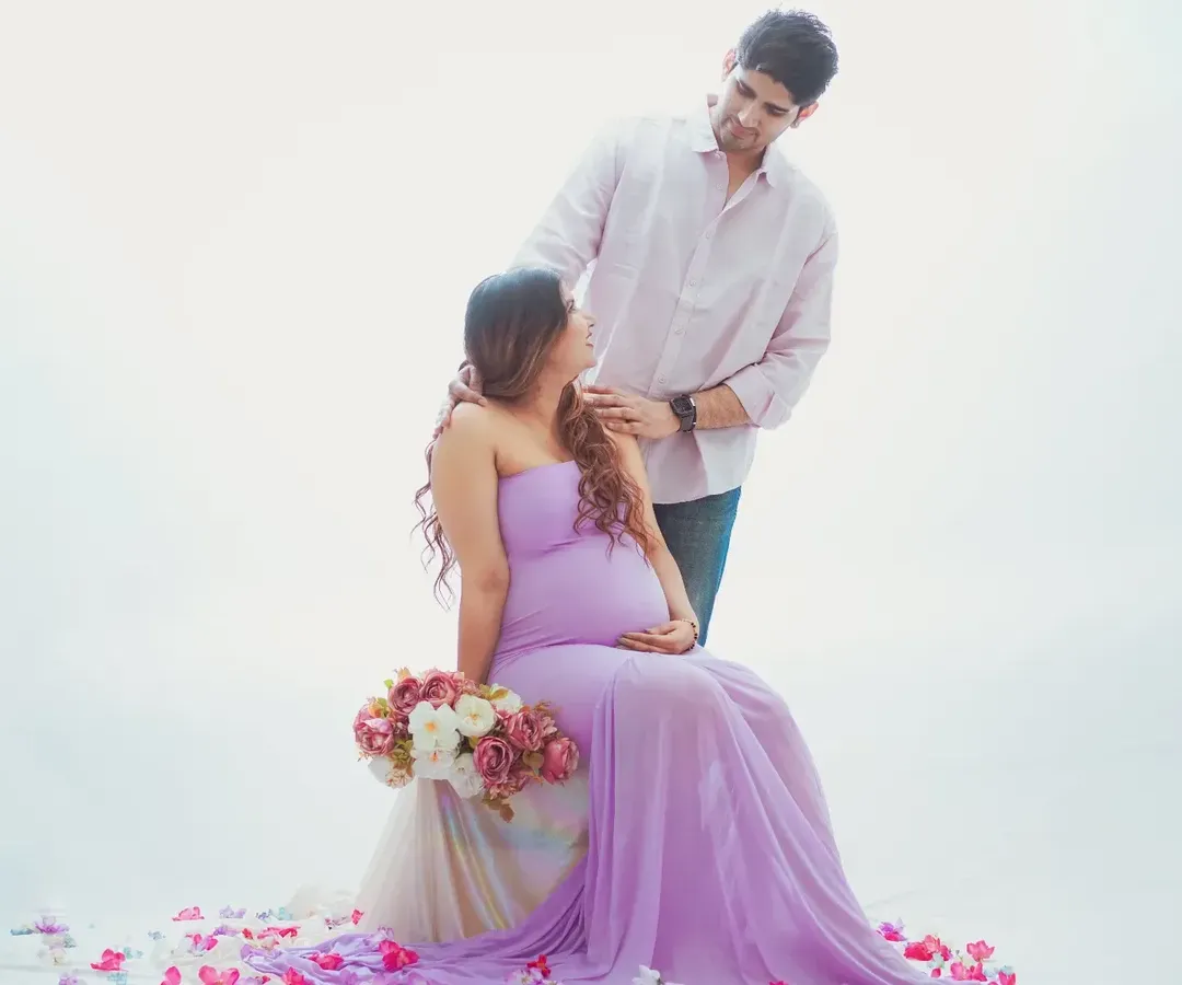 A romantic couple maternity shoot with a light and airy feel. The soft lavender gown and minimalist white background create a serene atmosphere, focusing on the connection between the expecting parents.