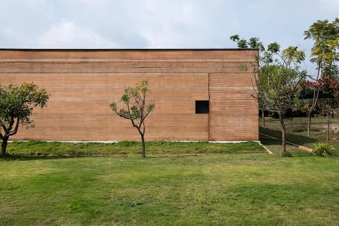 The monolithic rammed earth wall of the H.N. Science Center in Gauribidanur showcases the beauty of building with local soil. The horizontal layers tell the story of its construction, creating a facade that is both monumental and deeply connected to its site.