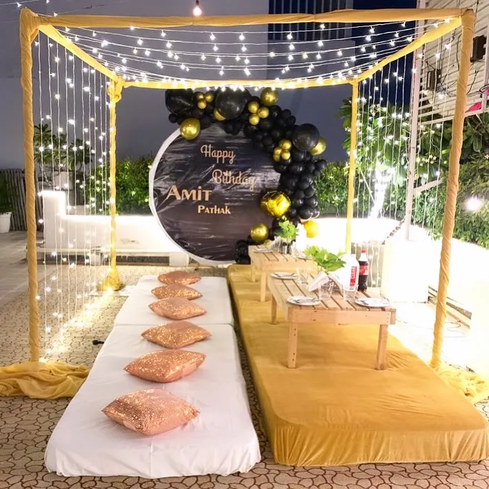 We create cozy and intimate experiences like this private cabana setup on a terrace. The arrangement includes low seating with plush cushions, a personalized "Happy Birthday" backdrop, and enchanting fairy lights, perfect for a romantic dinner under the stars.