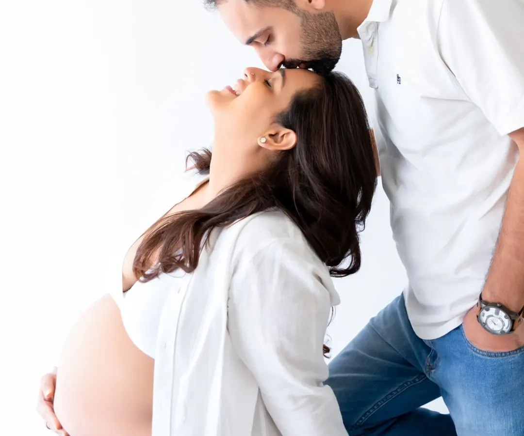 An intimate moment between expecting parents, captured in a bright, minimalist studio setting. This candid couple's pose highlights the connection and joy of pregnancy.