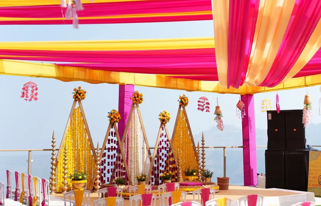 We bring vibrancy to tradition with setups like this stunning outdoor Haldi ceremony. The brilliant pink and yellow drapes create a joyful canopy, while the intricate marigold backdrops and floral arrangements set the stage for a day filled with laughter and blessings.