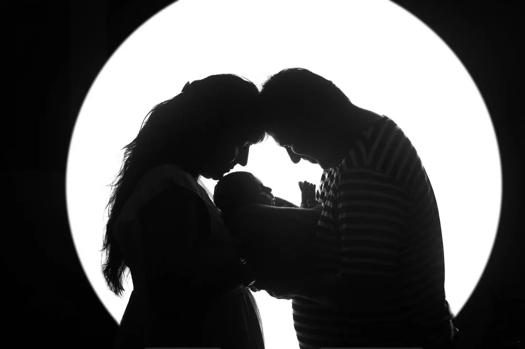 A powerful and artistic silhouette of new parents adoring their newborn. This black and white newborn portrait focuses on the emotion and bond of a new family.
