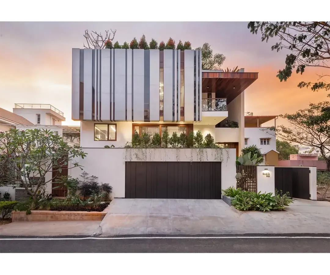The facade of the House Above The Tree captured at sunset, showcasing how the structure interacts with light. We used clean lines, a rooftop garden, and distinctive vertical louvers to create a modern home that is both private and open to its surroundings. This view highlights the home's strong geometric form against the soft evening sky.