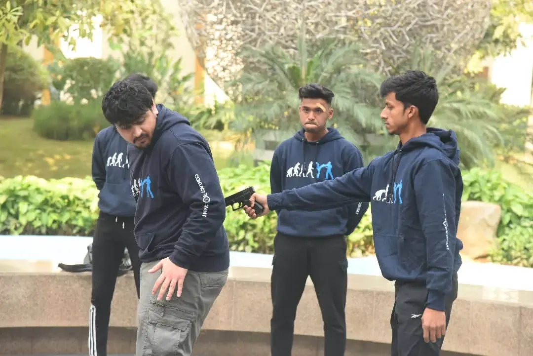A gun to your back is a worst-case scenario, and I train you for it. This image shows a gun defense drill, focusing on how to turn, redirect the weapon away from your body, and gain control when you have no other choice.