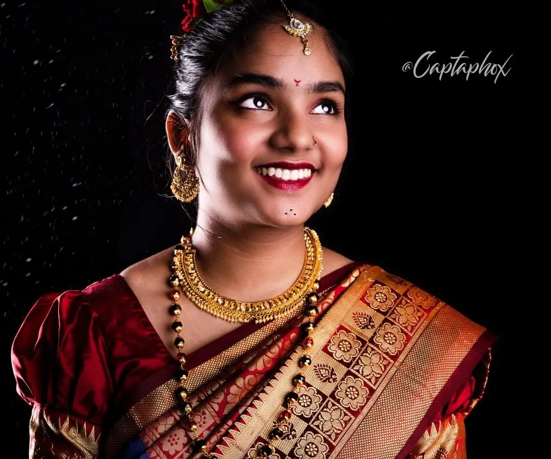 A joyful and elegant portrait capturing the beauty of a traditional Marathi look. I use a classic black background and specific lighting techniques to make the rich colors of the saree and the intricate gold jewelry stand out.
