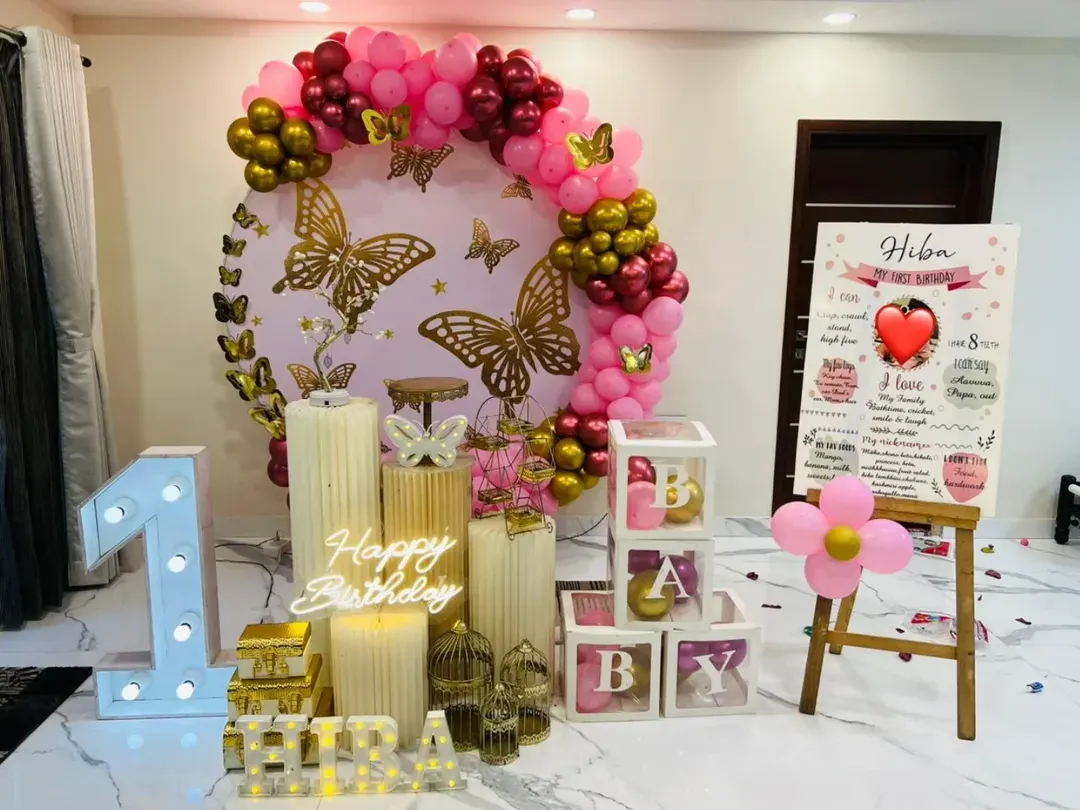I love creating magical first birthday setups like this butterfly theme. It features a large circular backdrop with golden butterflies, a pink and gold balloon garland, a light-up marquee '1', illuminated name and 'BABY' blocks, and a personalized milestone board detailing the baby's first year.