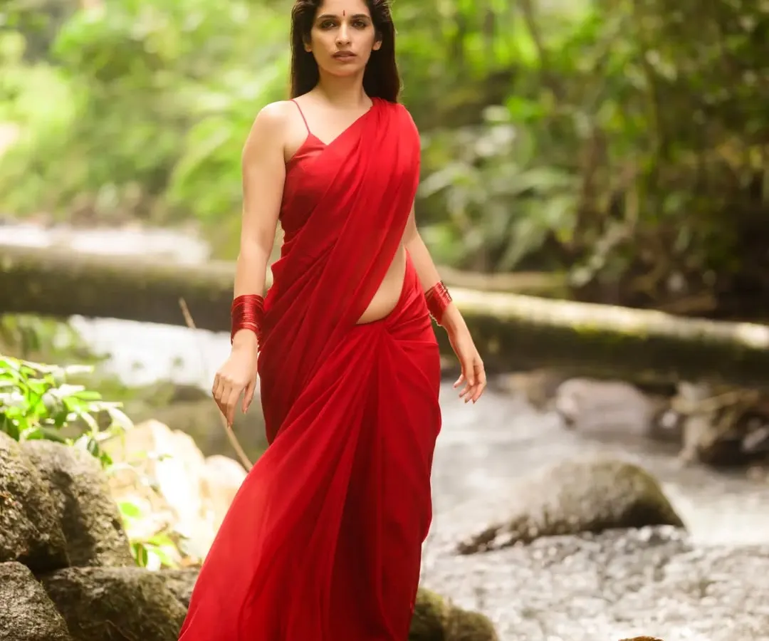 "Baanadi mooduva kalarava naanu!" I am the chirping that rises in the sky. For this outdoor portrait, we used the natural forest stream as a backdrop, letting the vibrant red saree stand out against the greens. This shot is all about capturing a story of being one with nature.