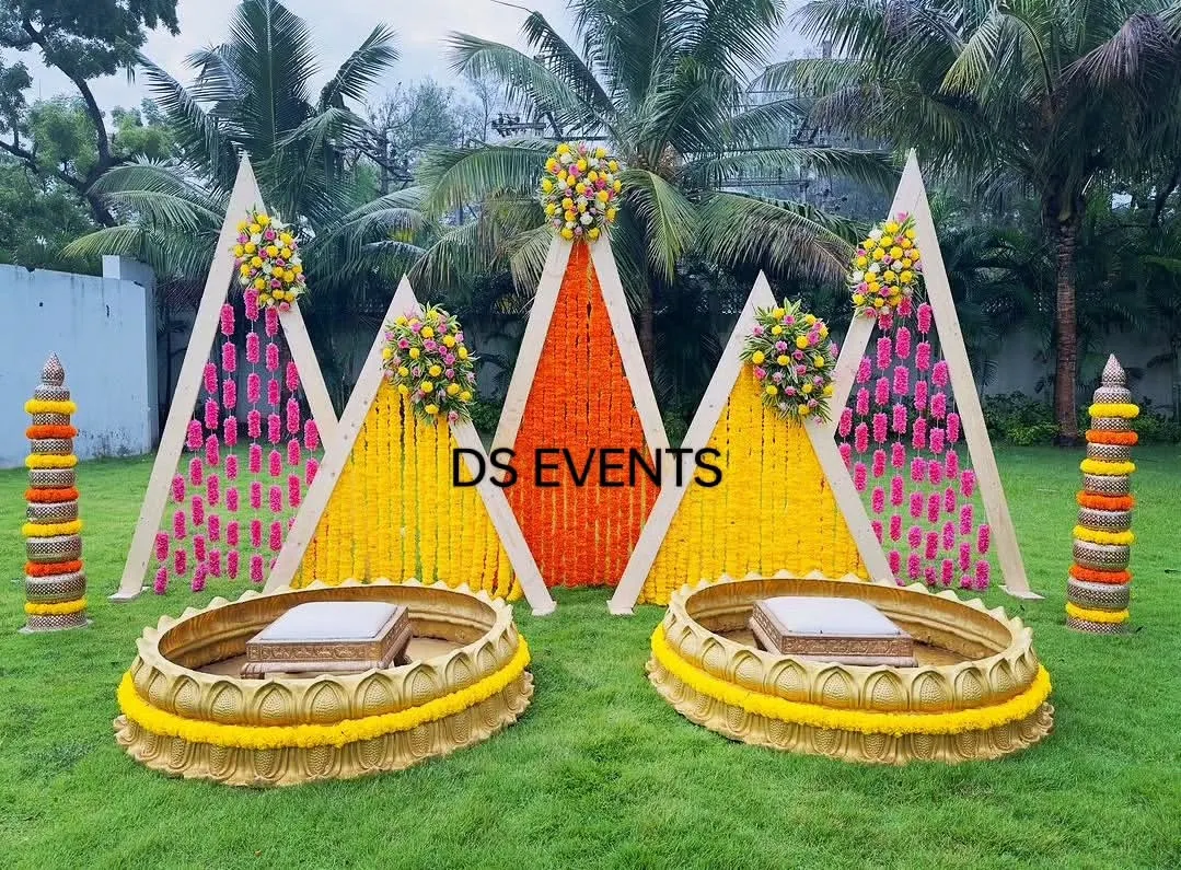 For this outdoor Haldi ceremony, I designed a vibrant setup using A-frame backdrops with marigold and tuberose flower hangings. The custom-made lotus-shaped urlis for the seating add a unique and traditional touch, making it perfect for photos.