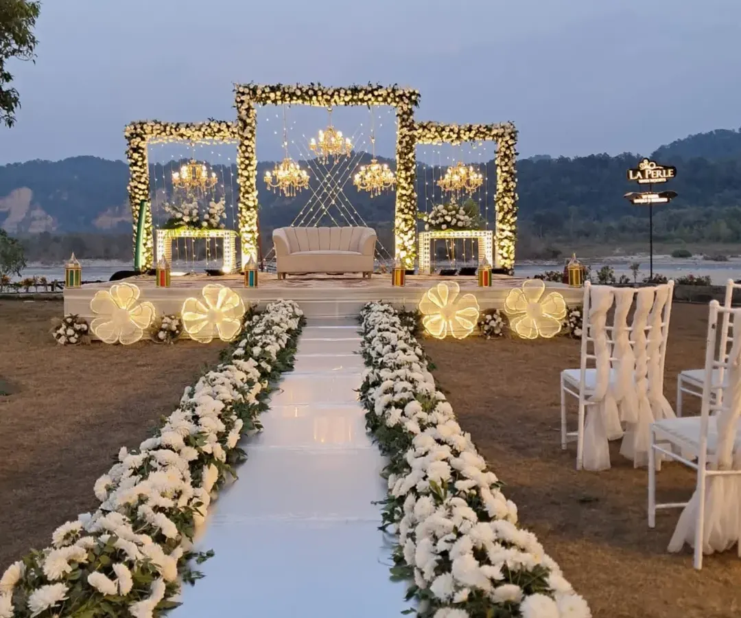 For a more elegant and sophisticated affair, I designed this stunning riverside engagement stage in Jim Corbett. The combination of white floral frames, grand chandeliers, and a clean white aisle creates a breathtaking focal point against the natural backdrop.