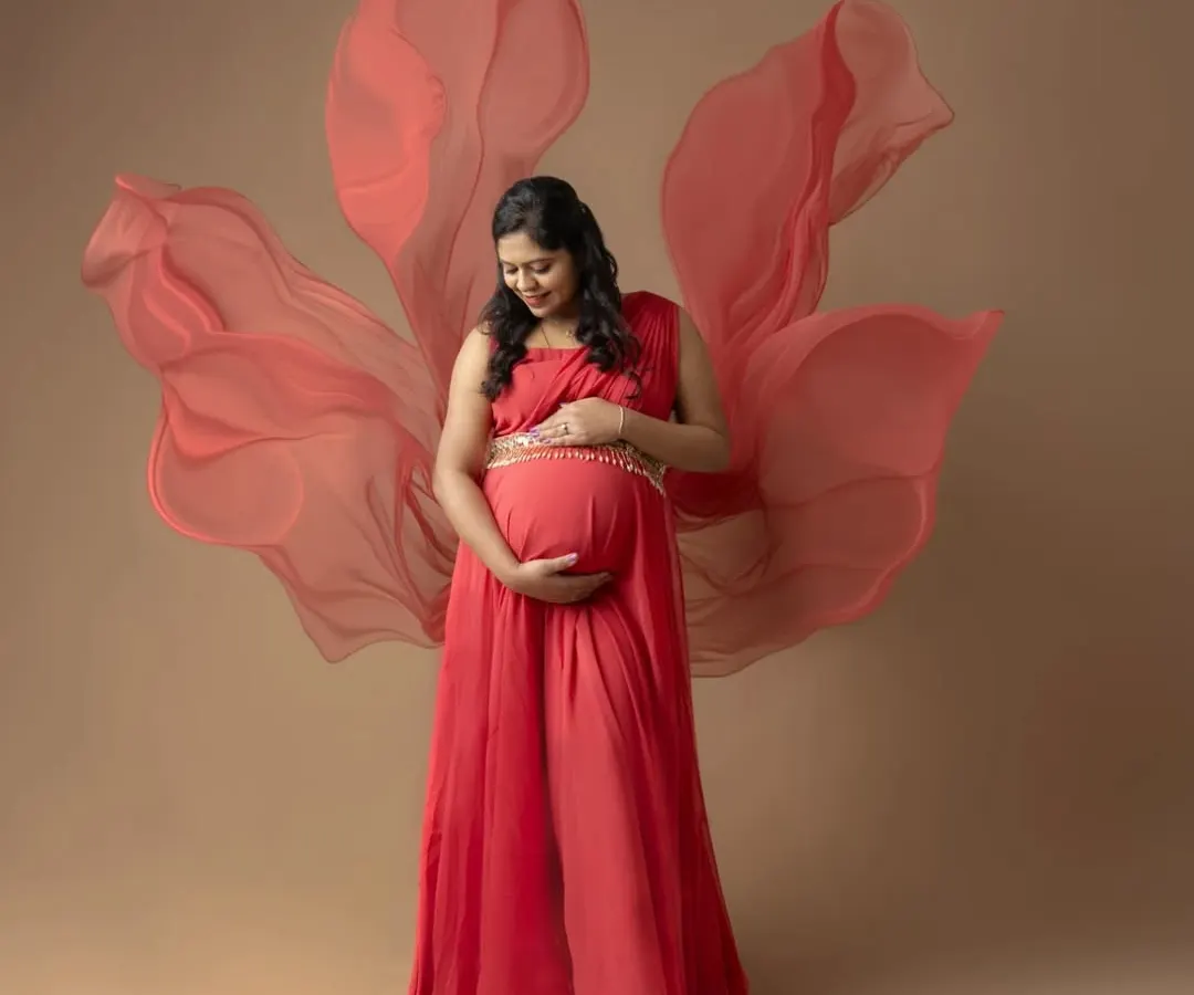 Embracing the goddess within. This portrait showcases the power and beauty of motherhood, using a flowing red gown and soft fabric to create a sense of dreamy elegance for a maternity photoshoot.