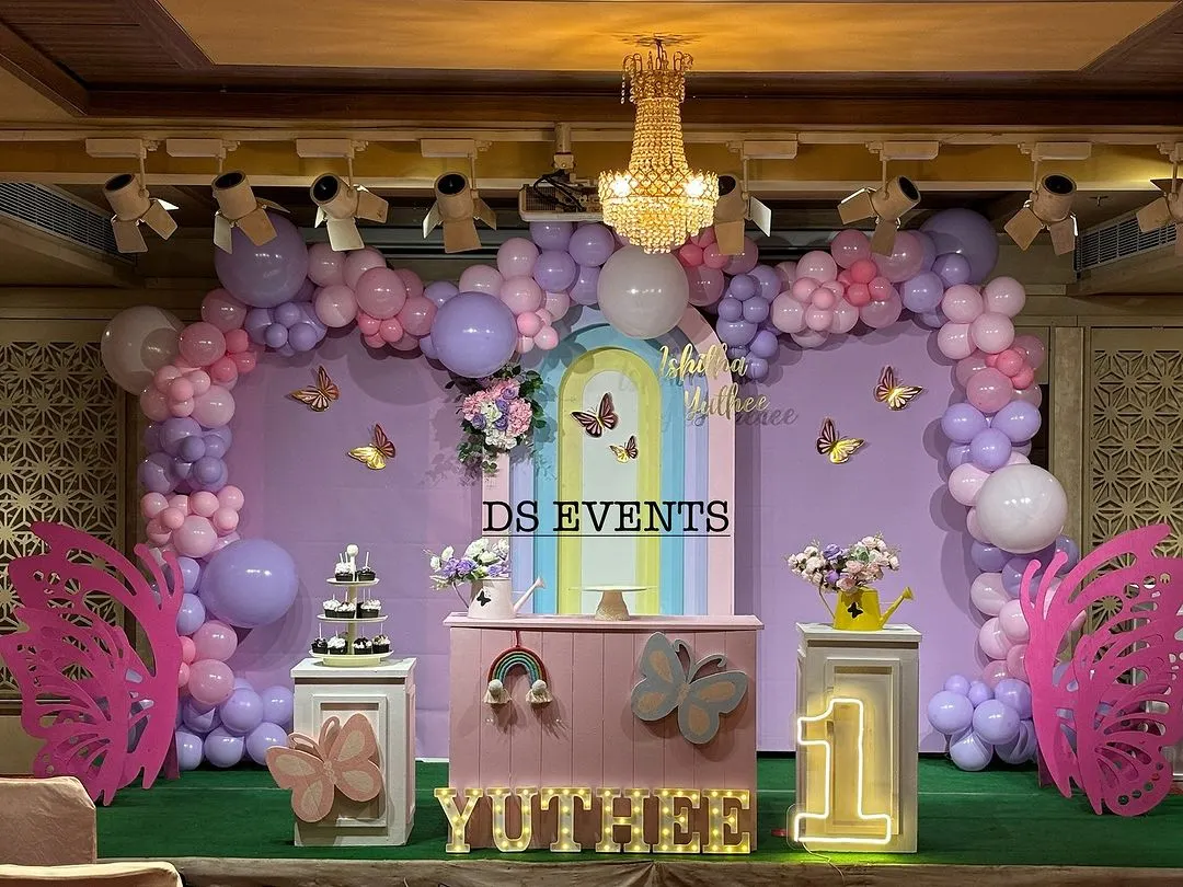 This is a full-stage butterfly theme I designed for a first birthday. It features a large pastel balloon garland, custom-painted backdrops, light-up marquee numbers, and themed props like the giant pink butterfly wings for a perfect photo opportunity.
