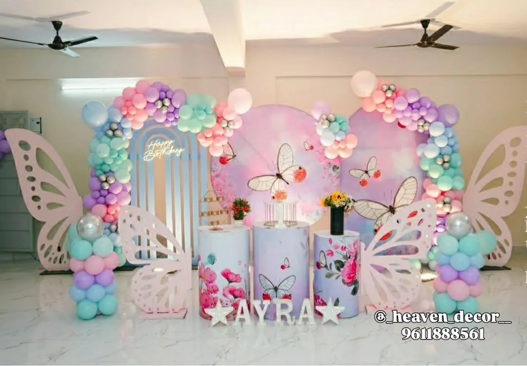 An enchanting butterfly-themed party with a pastel rainbow balloon arrangement. This setup includes large, freestanding butterfly wing props, custom-printed plinths, and a personalized backdrop, creating a magical atmosphere.