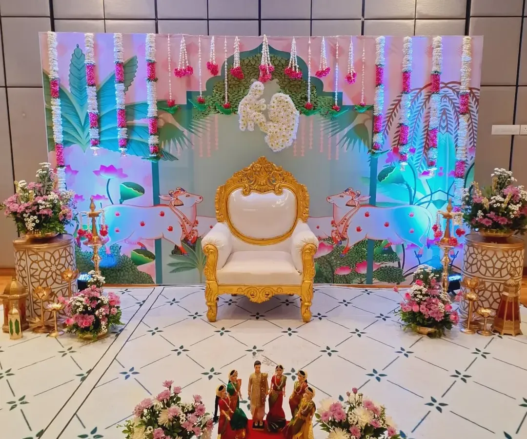 A complete stage setup for a Sreemantham, blending modern aesthetics with traditional touches. The elegant throne for the mother-to-be is the centerpiece, framed by a custom-printed backdrop, fresh flower garlands, and warm lighting to create a perfect photo opportunity.