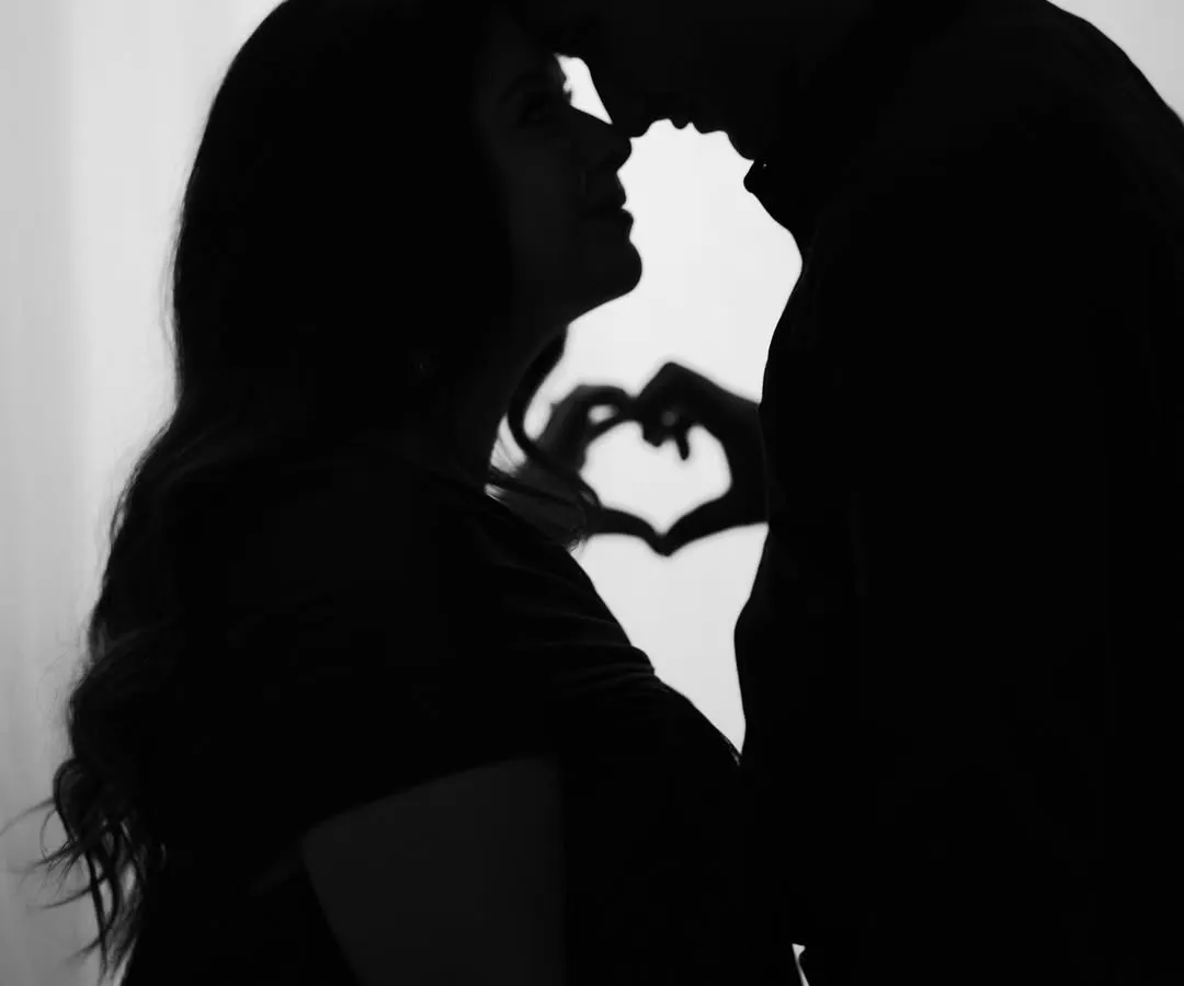 Sometimes the most powerful moments are the quietest. This artistic silhouette shot captures the intimate connection between expecting parents, with their hands forming a heart in the background, symbolizing the love that started it all.