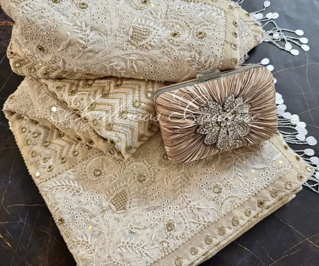 We present our heirloom Chikankari saree, a testament to opulent craftsmanship. Rendered on off-white crepe, this made-to-order piece is heavily highlighted with mirrorwork, Kutdana, and sequins, and is styled here with a complementary clutch for a complete festive look.