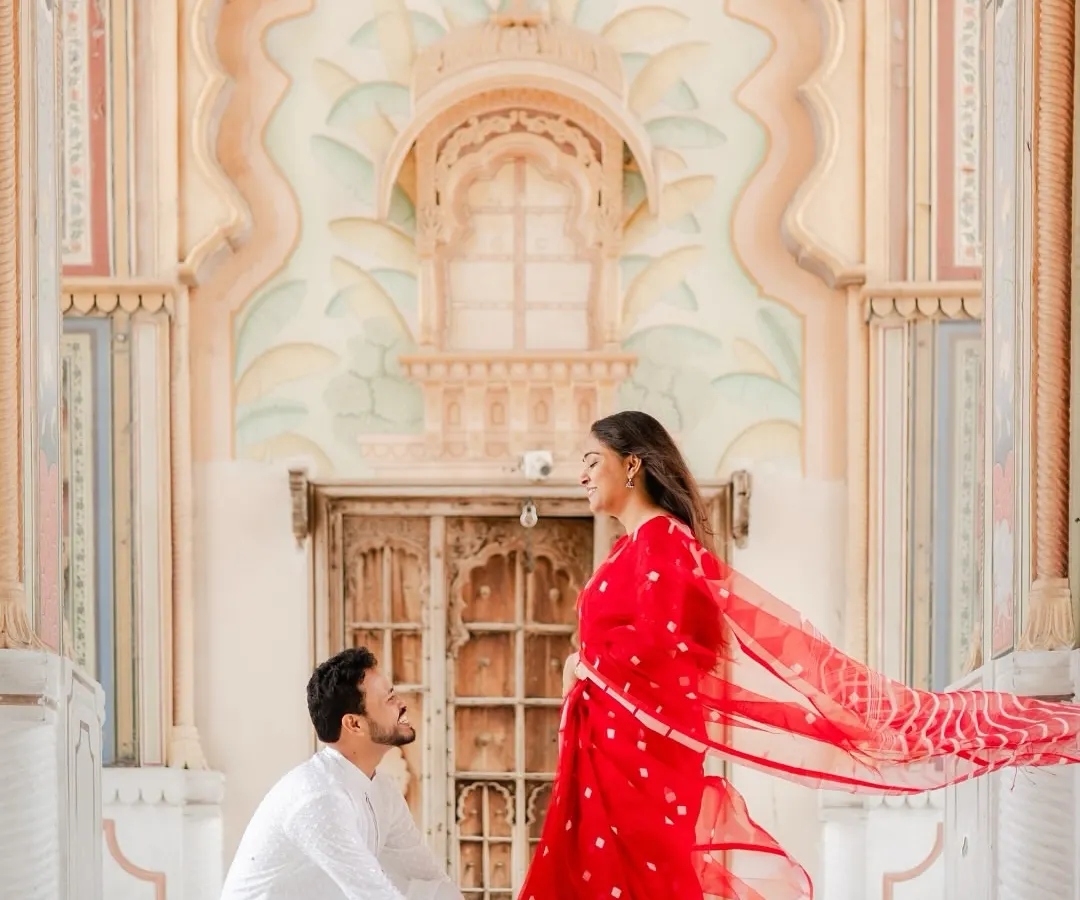 Against the magnificent arches of Jaipur's Patrika Gate, he asked for her forever. The vibrant red of her saree and the grandeur of the setting create a truly royal proposal photograph.