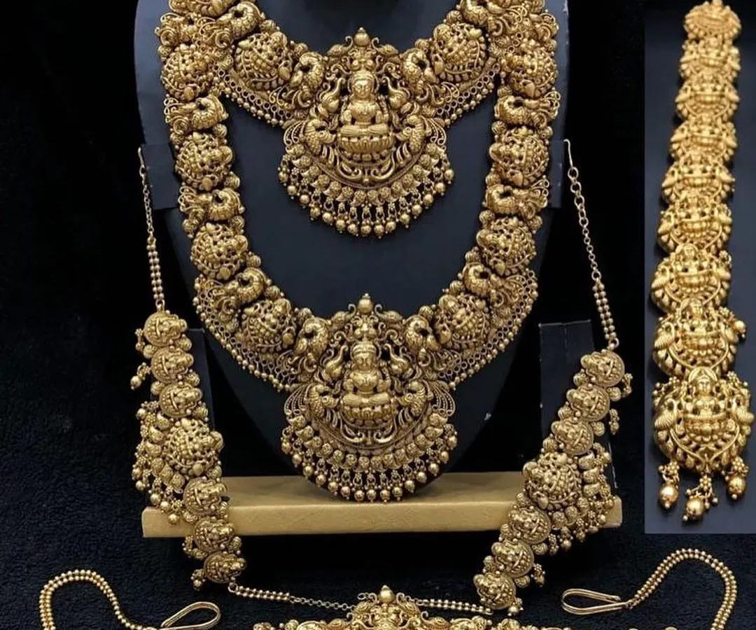 This is a full antique-finish temple jewellery set, perfect for achieving a classic bridal look. The set includes a choker, a long haaram, matching jhumkas, a vaddanam (waist belt), and hair accessories, all featuring intricate deity and peacock motifs.