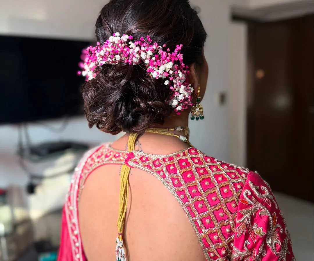 This is one of my signature styles, a soft, textured low bun woven with vibrant pink and white baby's breath. It's a romantic and popular choice for brides and bridesmaids, adding a beautiful pop of color that can be customized to match any outfit.
