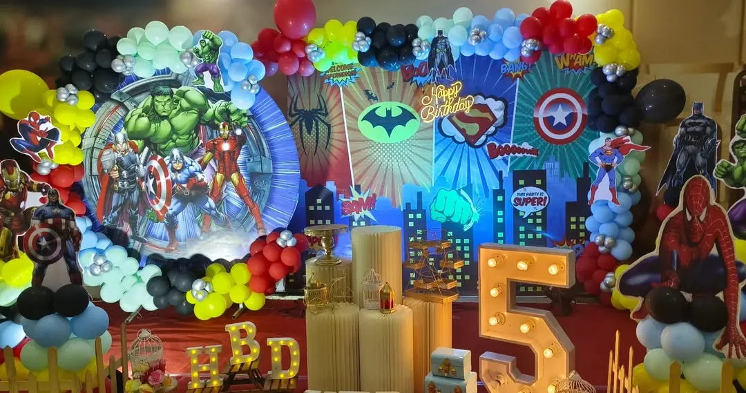 For the ultimate superhero fan, I created this action-packed Avengers birthday party stage. The setup features a dynamic city skyline backdrop, multiple superhero cutouts including the Hulk and Iron Man, themed balloon arrangements, and a large light-up number '5'.