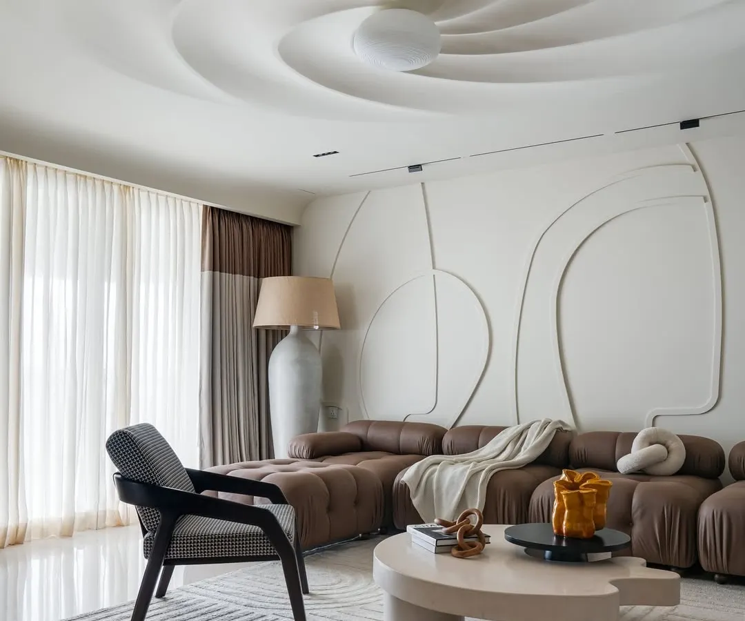 In this residential living room, the ceiling becomes a sculptural centerpiece. The swirling form creates a sense of movement and draws the eye upward, transforming a flat surface into a dynamic work of art. This feature, combined with the abstract wall molding, establishes a bold and eccentric personality for the home.