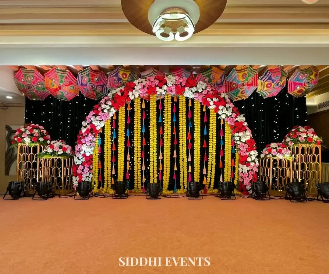 We designed this spectacular stage for a vibrant Haldi ceremony. A canopy of colorful Rajasthani umbrellas and a dramatic black backdrop make the floral arch and hanging marigold garlands pop, creating a truly grand and festive focal point for the event.